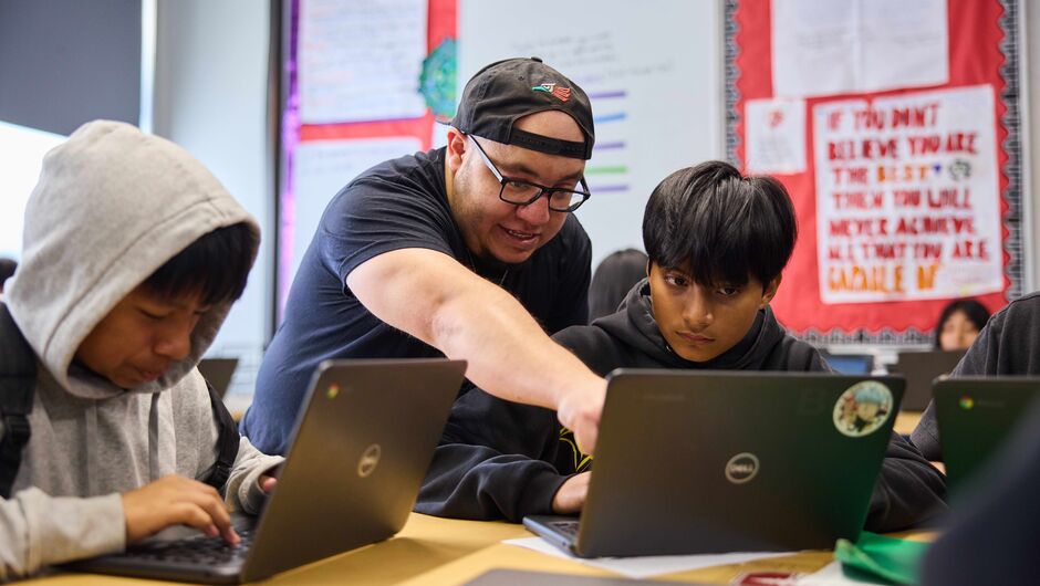 A male teacher works with a student on a computer.