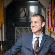 A man wearing a suit seated in a state capital building.