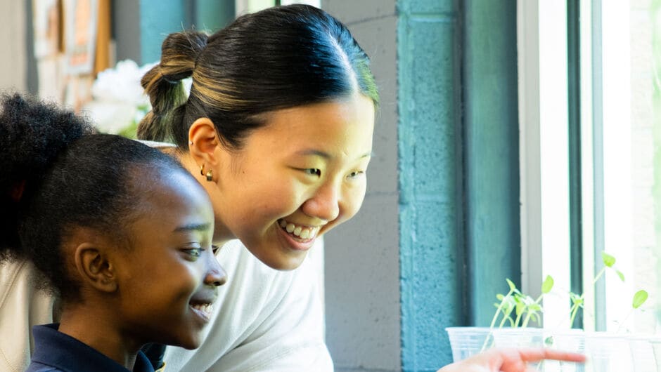 A teacher and student smile together looking at a growing plant