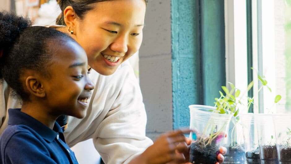 Student happily holding a plant next to her teacher