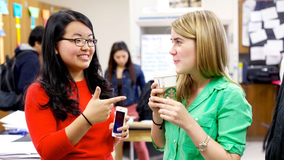 Two teachers talking while holding coffee and a phone