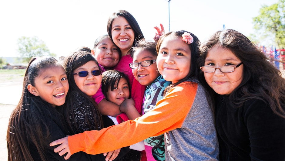 A teacher is surrounded in a big hug by several smiling students