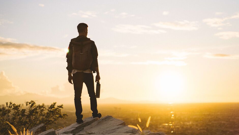 A person holding a water bottle and wearing a backpack looks over the sunrise in Phoenix.