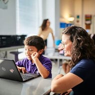 An educator works with a student at a laptop.