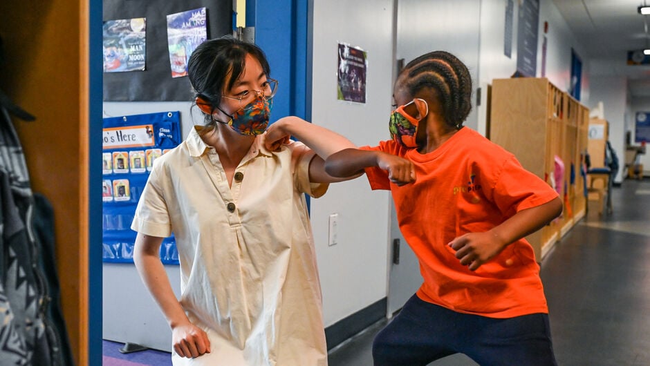 Teacher and student bump elbows in the school hallway. Both are wearing face masks.