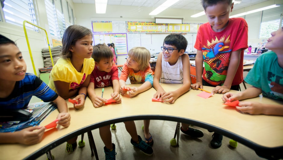 Alt text: Young students sit around a table in a classroom.