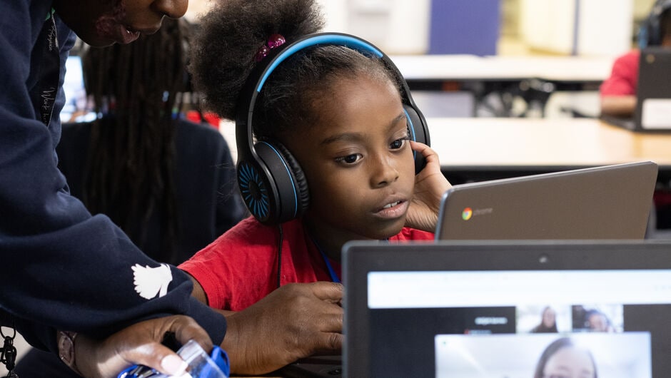 Alt text: a teacher helps a student with a laptop.