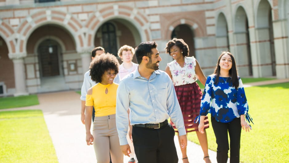 A group of young people walk across a college campus.