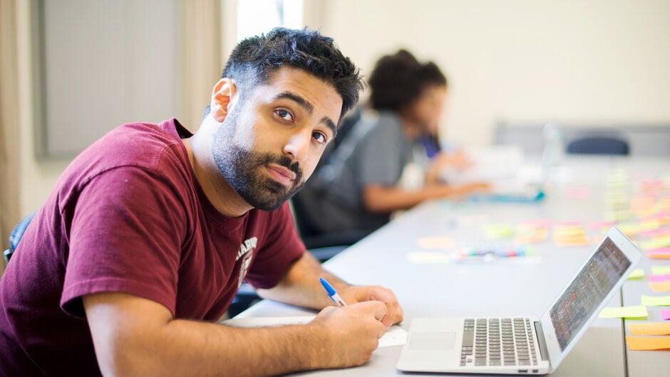 person on desk taking notes in front of laptop