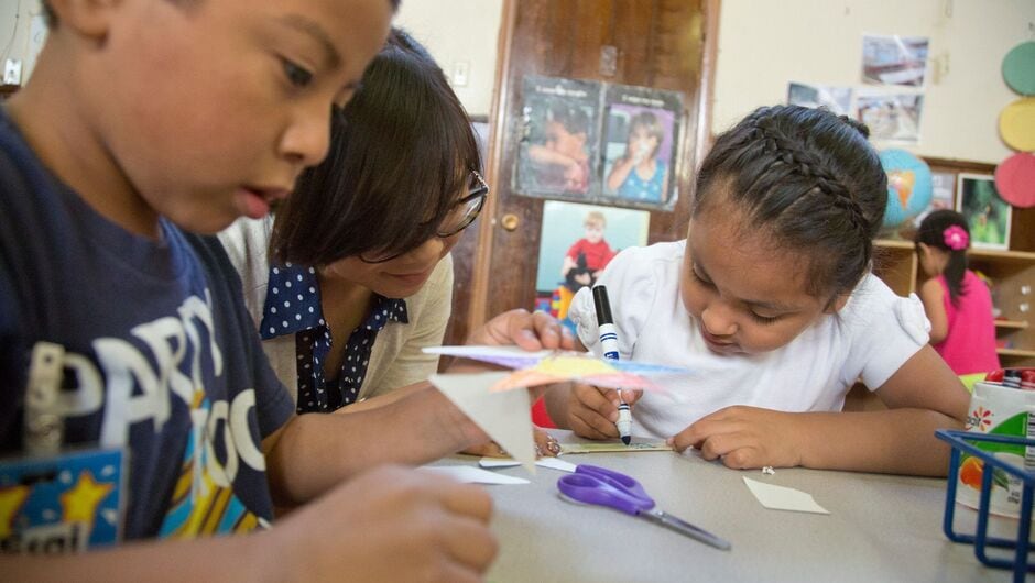 Alt text: A teachers helps students with an activity at a classroom table.