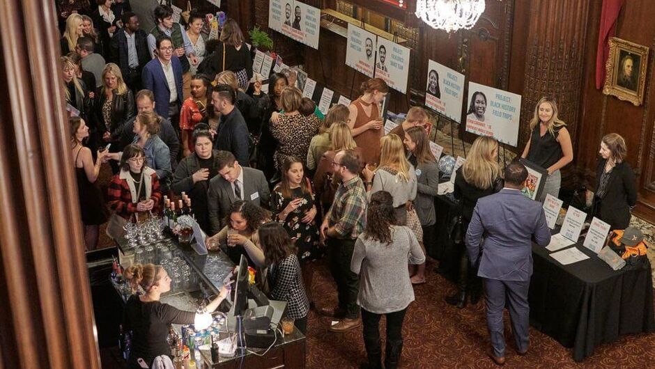 people crowd around tables and chat happily at an event